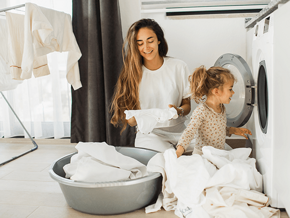 Fomentar la responsabilidad en los niños Madre e hija al lado de un lavarropas, con ropa blanca alrededor.