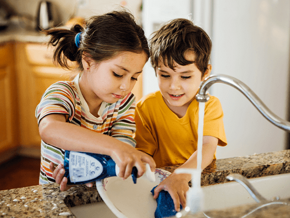 Niña y niño lavando un plato en la cocina.