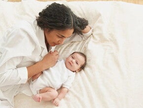 Mamá acostada en la cama con su bebé de 3 meses.