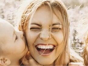 Hijo pequeño dando un beso en el cachete a mamá quien sonríe 