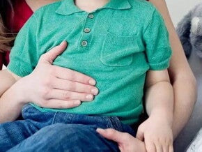 Mamá poniendo su mano sobre la barriguita de un niño pequeño intolerante a la lactosa.