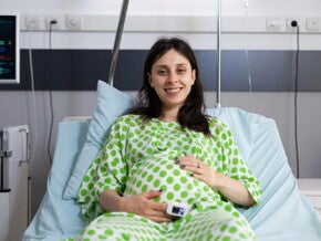 Mujer embarazada sonriendo, usando una bata de hospital y acostada en una camilla.