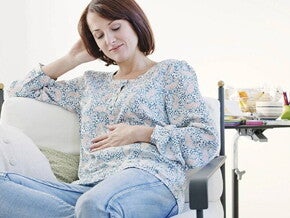 Primer mes de embarazo Mujer embarazada de un mes, sentada en un sofá, acariciando su vientre y sonriendo.
