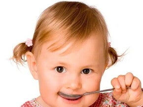 Niña pequeña comiendo con una cuchara alimentos con hierro.