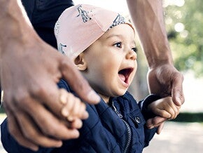Papá agarrando las manos de su bebé dando sus primeros pasos