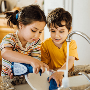 Niña y niño lavando un plato en la cocina.