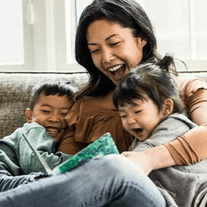 Madre y dos niños pequeños sentados en un sofá, leyendo un cuento, sonriendo.