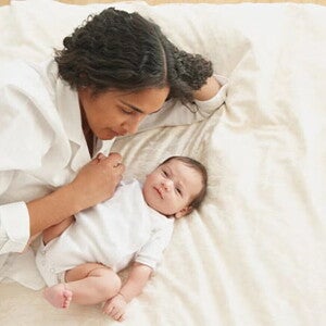 Mamá acostada en la cama con su bebé de 3 meses.