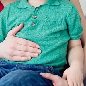 Mamá poniendo su mano sobre la barriguita de un niño pequeño intolerante a la lactosa.
