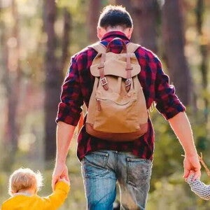 Papá agarrando a sus dos hijos en cada mano, caminando por un bosque soleado.