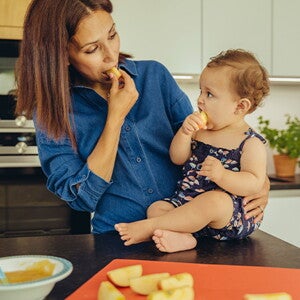 Mamá y bebé comiendo fruta en la cocina.