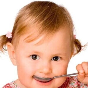 Niña pequeña comiendo con una cuchara alimentos con hierro.