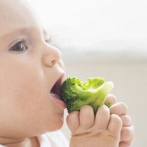 Imagen de un adorable bebé disfrutando de una comida saludable mientras come brócoli Imagen de un adorable bebé disfrutando de una comida saludable mientras come brócoli