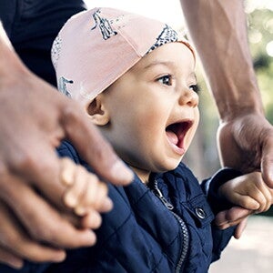Papá agarrando las manos de su bebé dando sus primeros pasos
