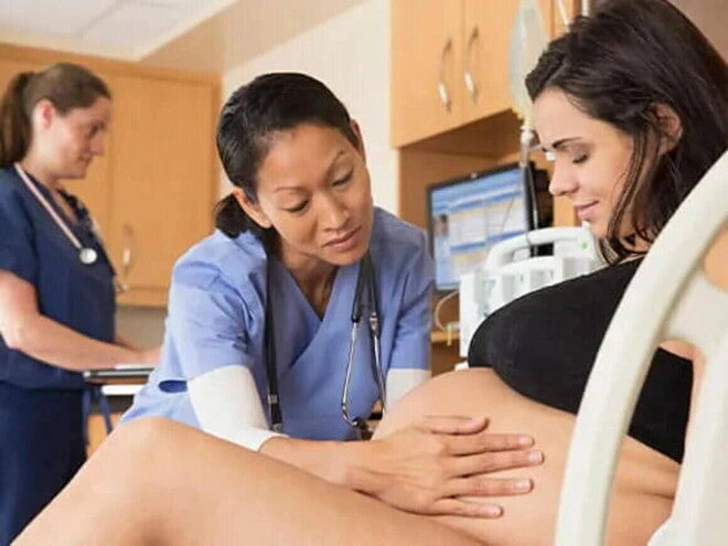 Mujer en trabajo de parto acostada en la camilla de hospital, sonriendo y con una doctora acariciando su vientre.