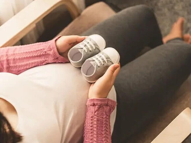 Conoce qué es el bebé arcoíris. Mamá embarazada de un bebé arcoíris cogiendo unos zapatitos.