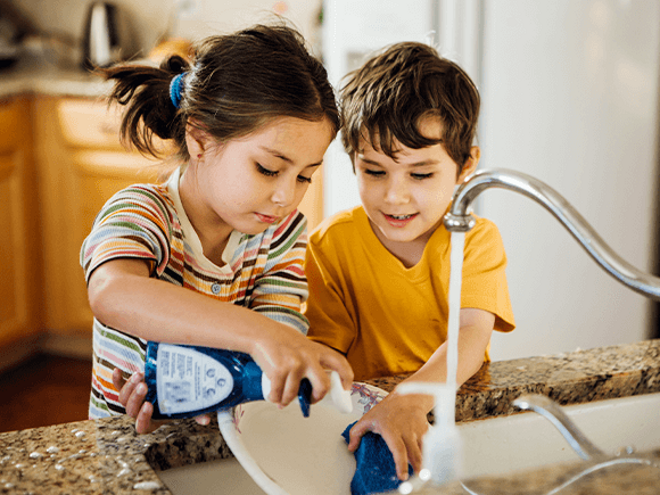 Niña y niño lavando un plato en la cocina.