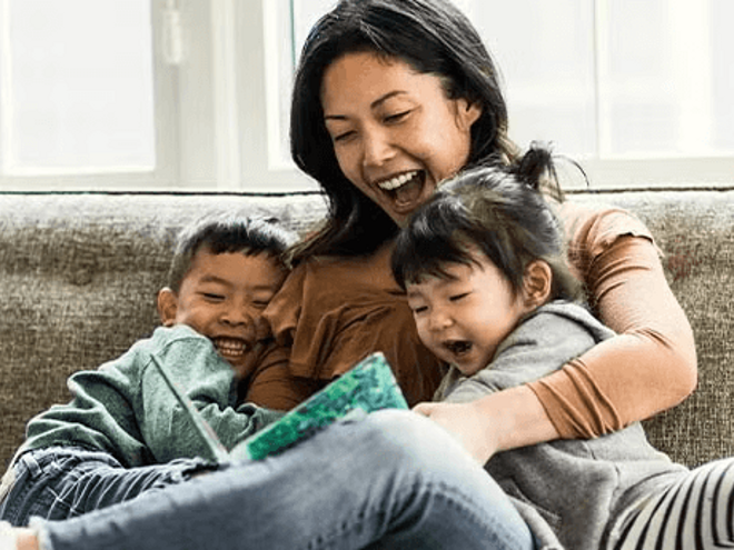 Madre y dos niños pequeños sentados en un sofá, leyendo un cuento, sonriendo.