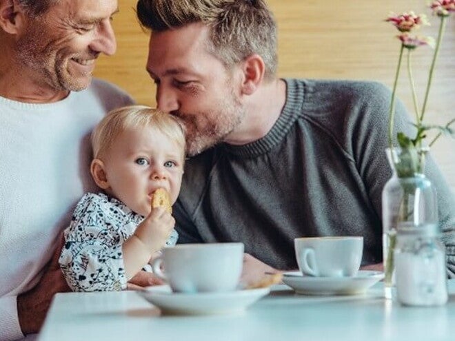 Conoce cuándo puedes darle galletas para bebés a tu hijo. Niña comiendo galletas para bebés con su papá y abuelo.