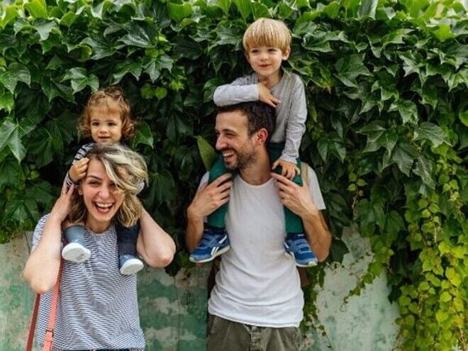 Estilos de crianza para educar a mi hijo. Los padres riendo con los hijos alzados.