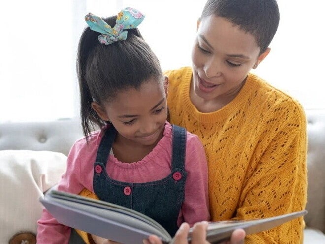 Mamá sentada en un sofá con su hija pequeña leyendo cuentos para niños