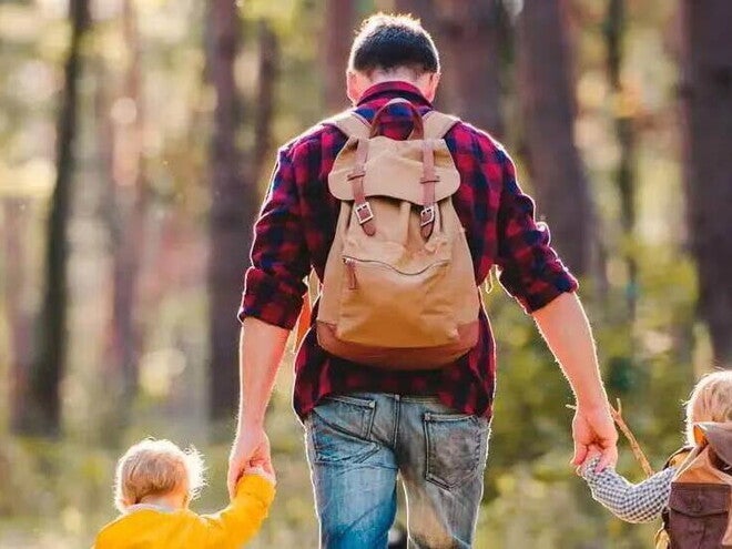 Papá agarrando a sus dos hijos en cada mano, caminando por un bosque soleado.