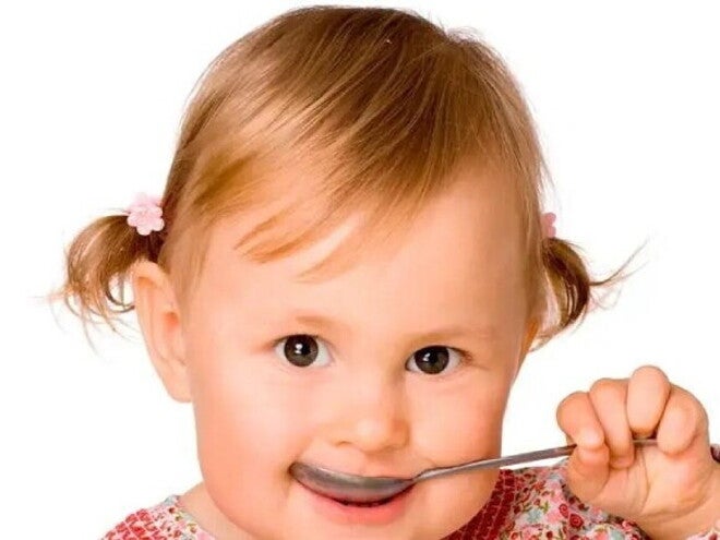 Niña pequeña comiendo con una cuchara alimentos con hierro.
