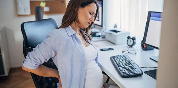 Identifica cuál es la diferencia entre preeclampsia y eclampsia. Mujer embarazada sentada sintiendo molestias.