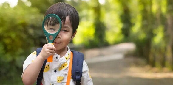 Mientras la motricidad fina desarrolla habilidades con escribir, la gruesa impulsa los movimientos grandes. Niño jugando con una lupa.