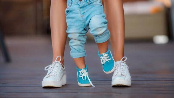 Pies de niño pequeño caminando y su mamá detrás.