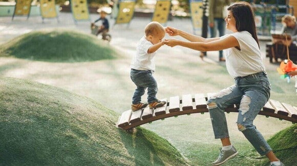 Mamá ayuda a su hijo pequeño a cruzar un puente en un parque de juegos para niños.